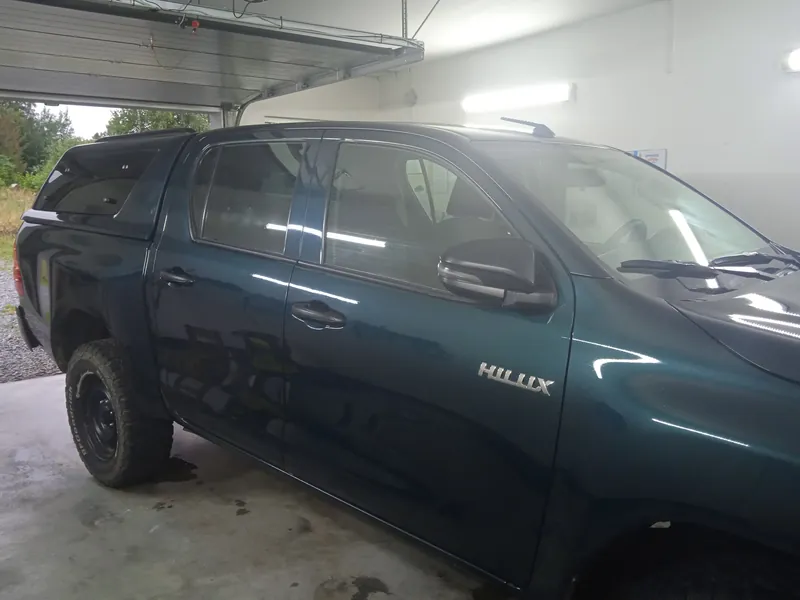 Tmavě zelený pickup s hardtopem stojí bokem k objektivu v garáži, lak i skla jsou čisté a lesklé.